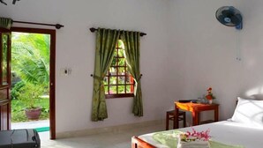 A hotel room with a bed, a desk, a chair, a window with curtains, and a ceiling fan. - Diem Lien Guesthouse (Mui Ne)