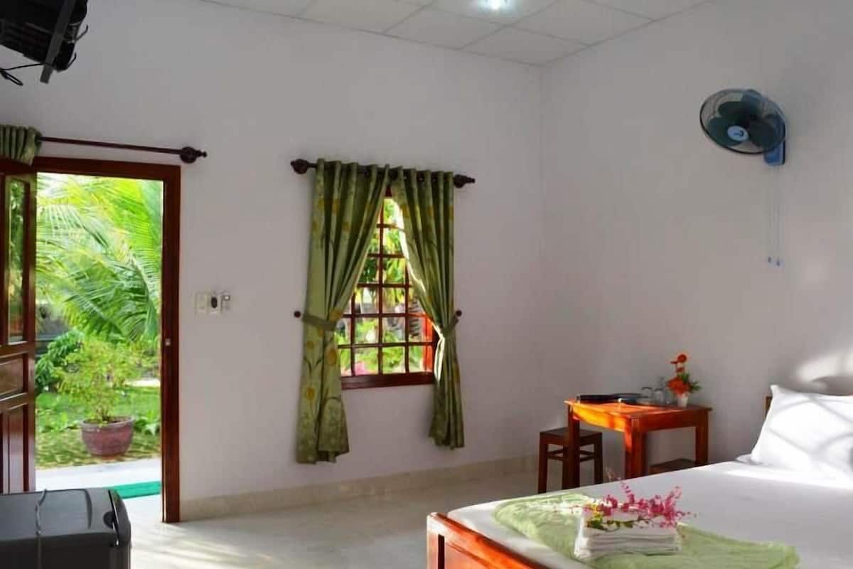 A hotel room with a bed, a desk, a chair, a window with curtains, and a ceiling fan.