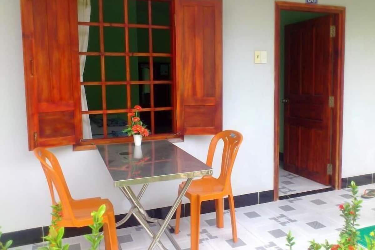 A room with a glass-top table, two orange chairs, a wooden door, and a window with wooden shutters.