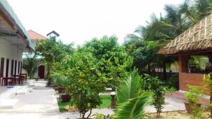 A courtyard with a thatched-roof structure, potted plants, and a pathway leading to a building with a red roof. - Diem Lien Guesthouse (Mui Ne)