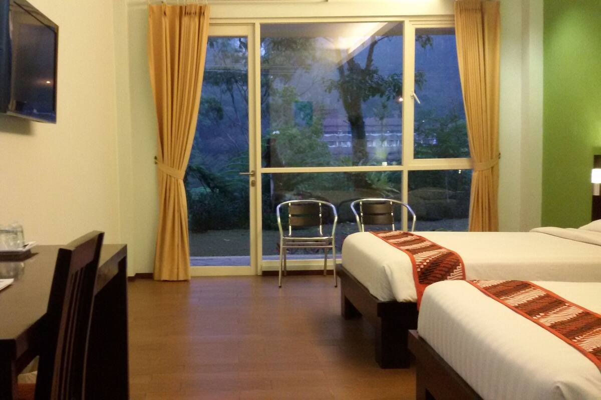 A hotel room with a bed, a desk with a chair, a TV, and a window with curtains.