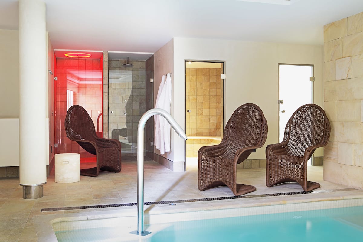Un espace piscine comprenant trois fauteuils en osier, une douche fermée par des parois de verre et une porte donnant sur une pièce avec une baignoire.