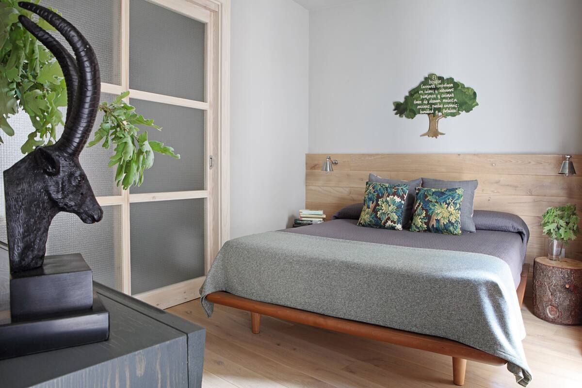 Une chambre à coucher avec une tête de lit en bois, une couvre-lit grise et des coussins décoratifs.