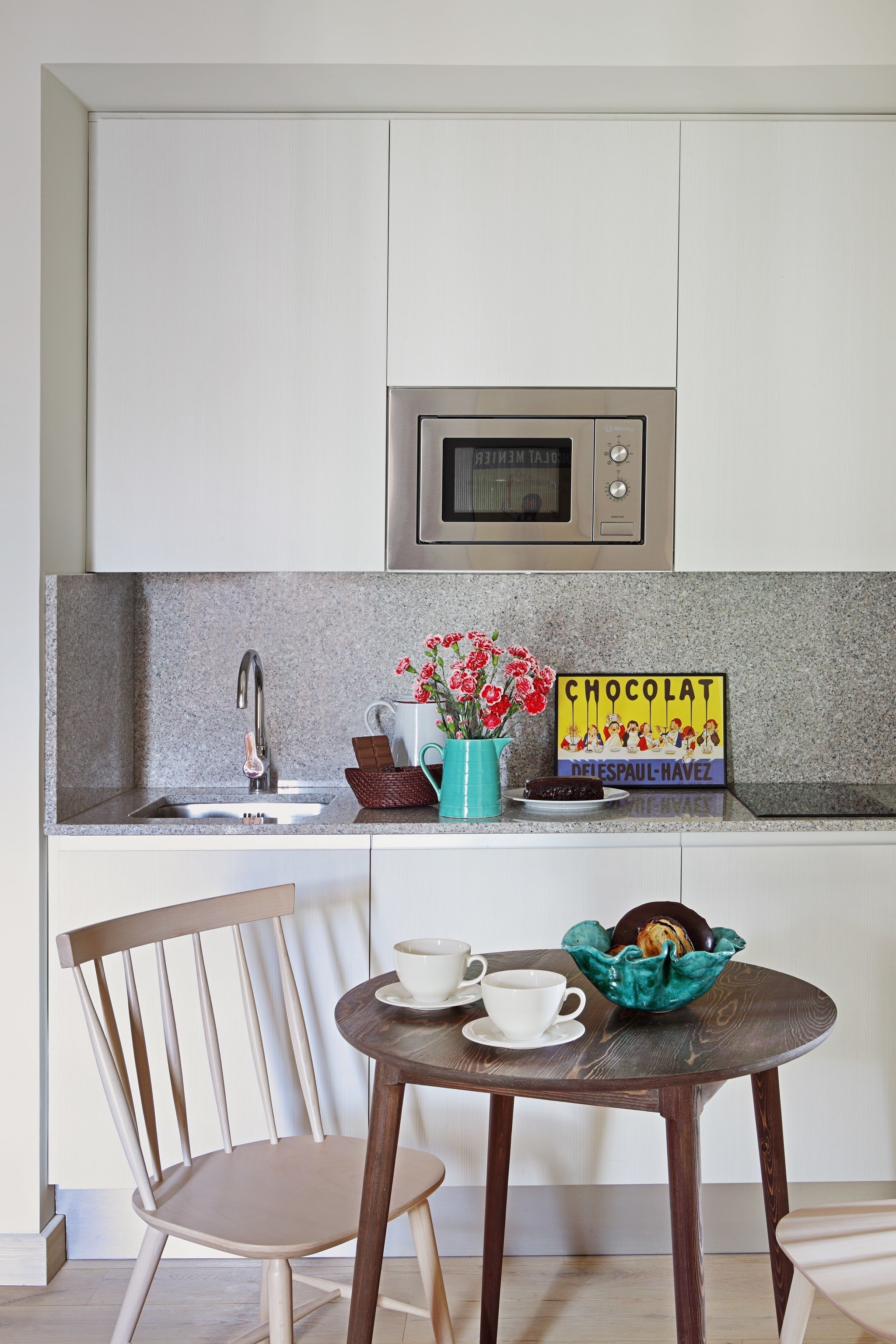 A kitchen with a microwave, a sink, and a table with a cup and a basket.