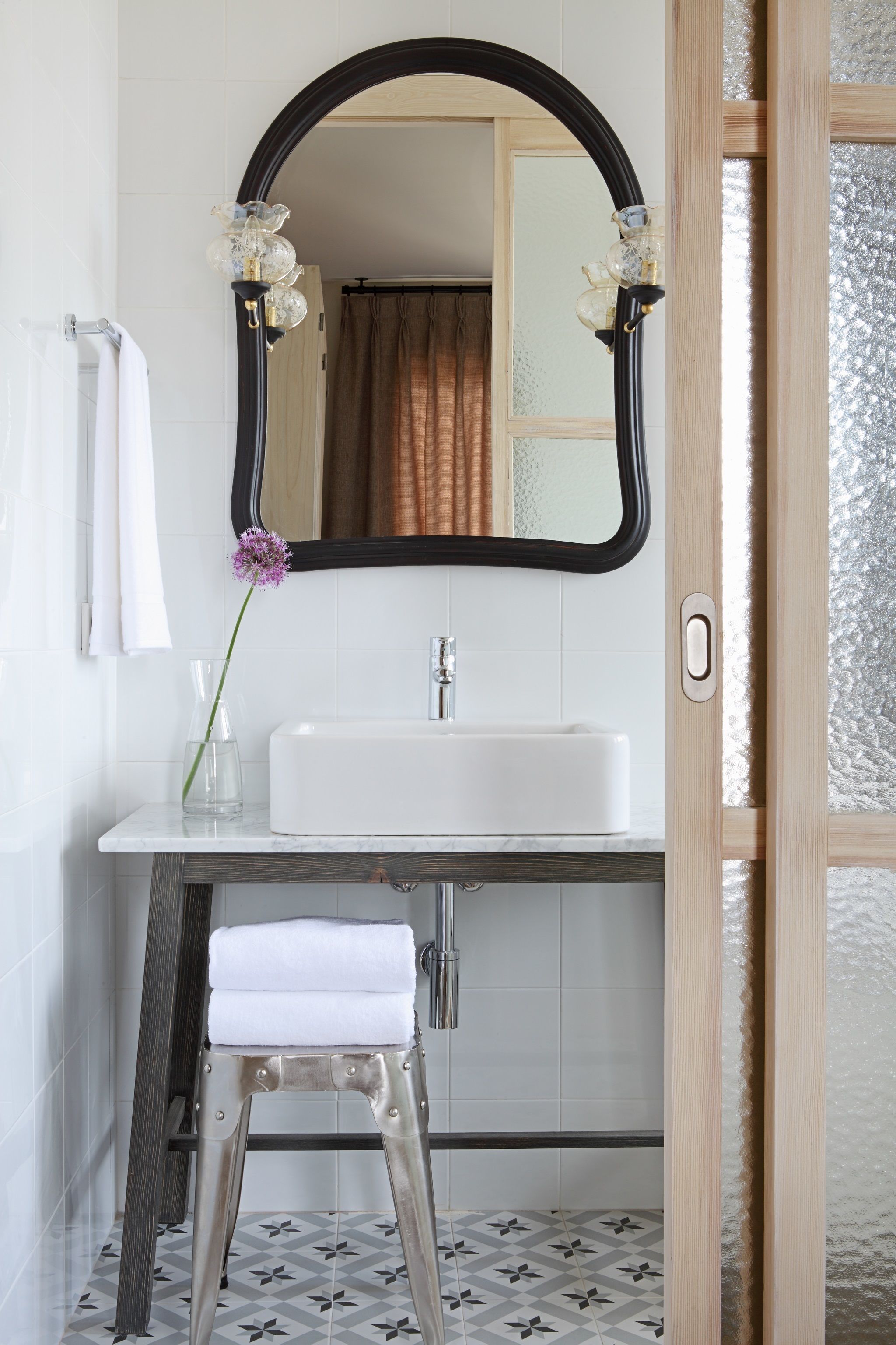 A bathroom with a white sink, a mirror, and a stool.