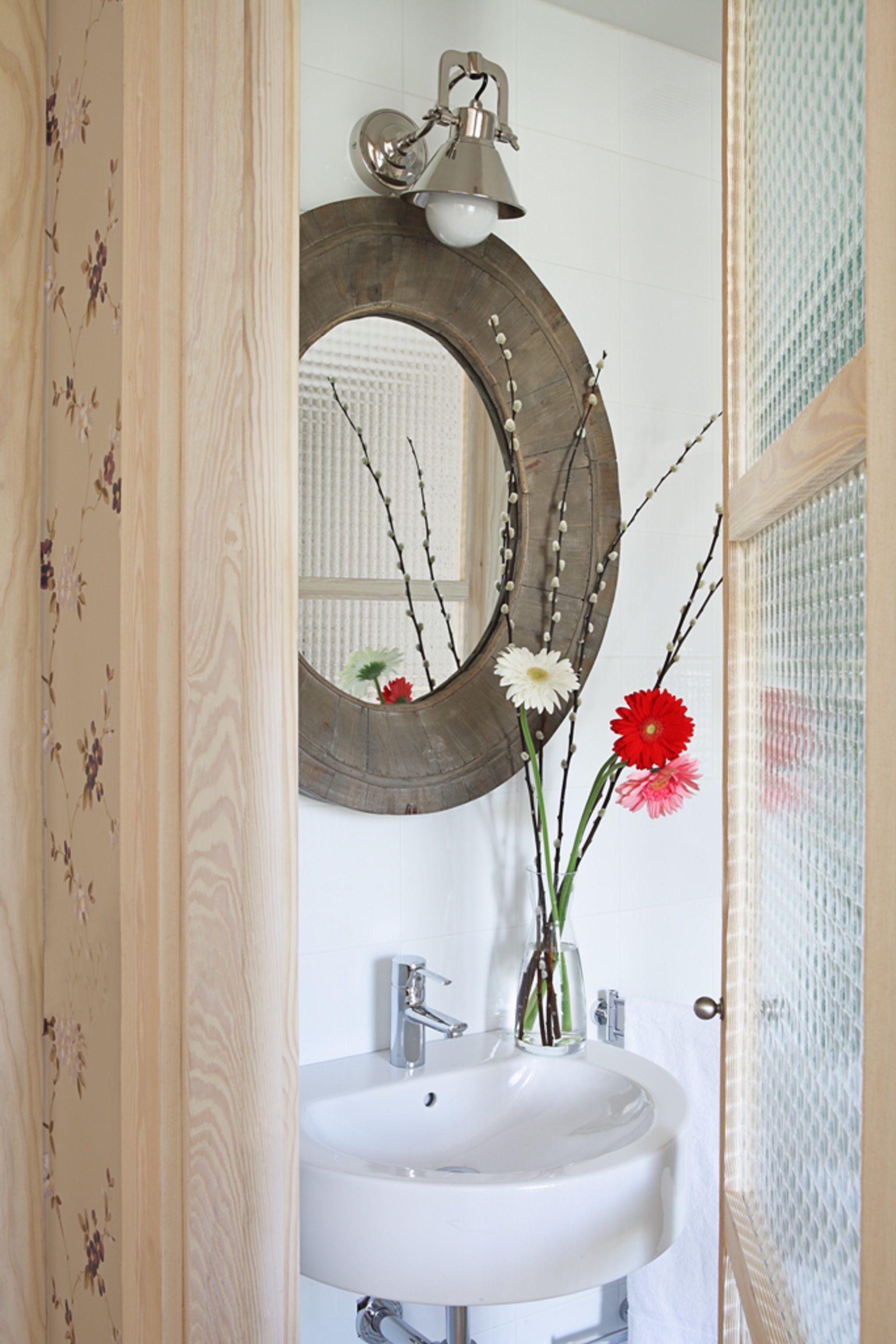 Une salle de bain avec un miroir encadré en bois, un lavabo blanc et un luminaire décoratif.