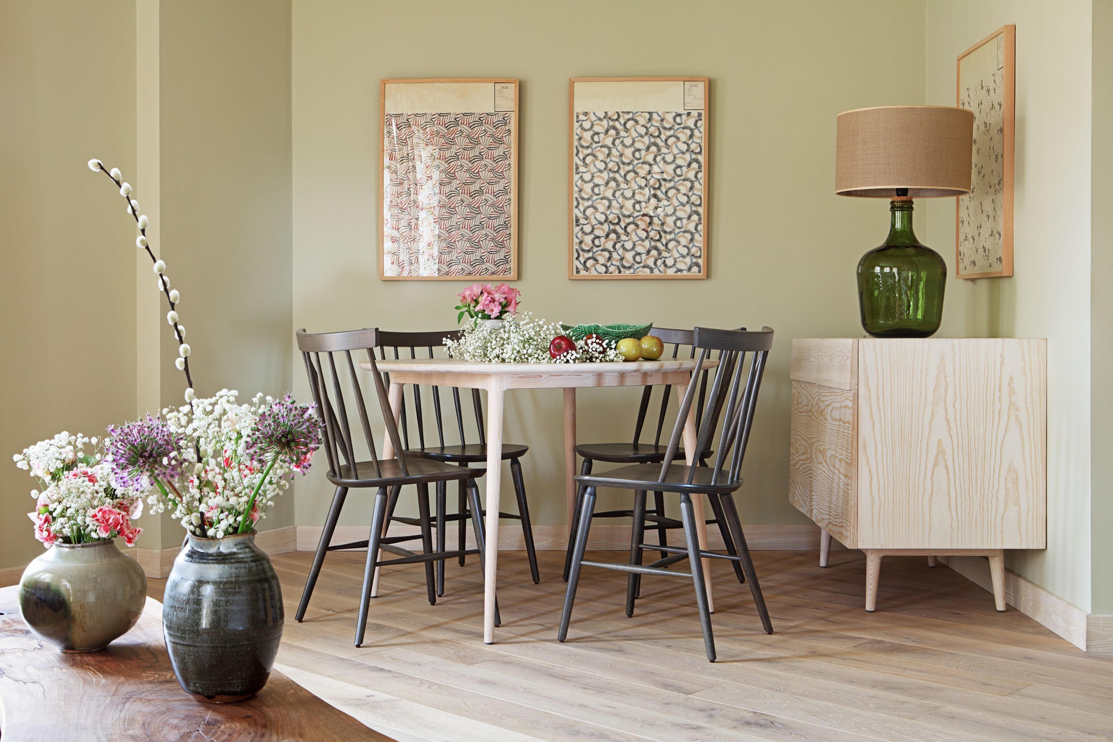 A dining area with a table and chairs, a vase with flowers, and two framed artworks on the wall.