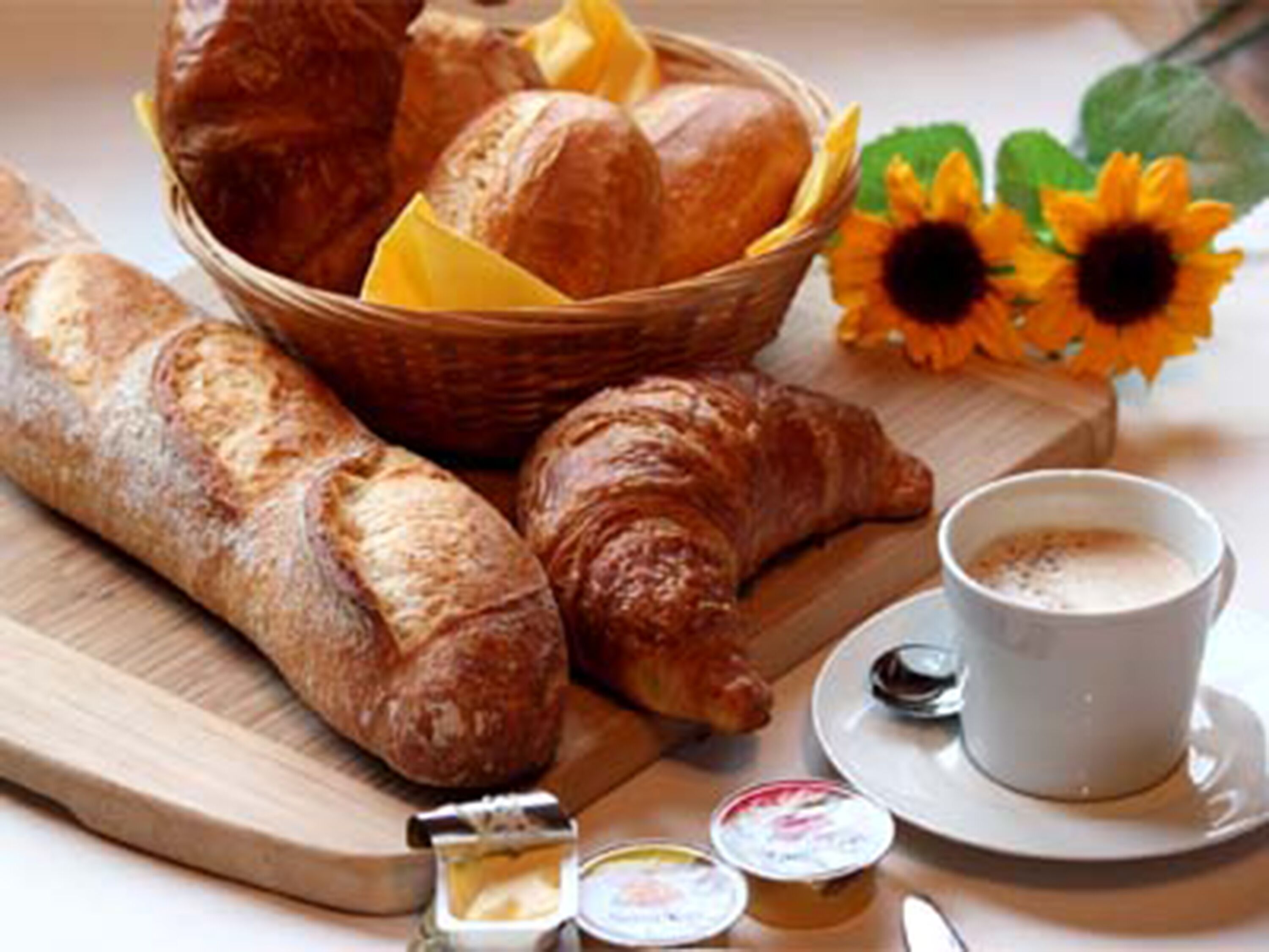 Un desayuno con pan, cruasanes, mantequilla y una taza de café.