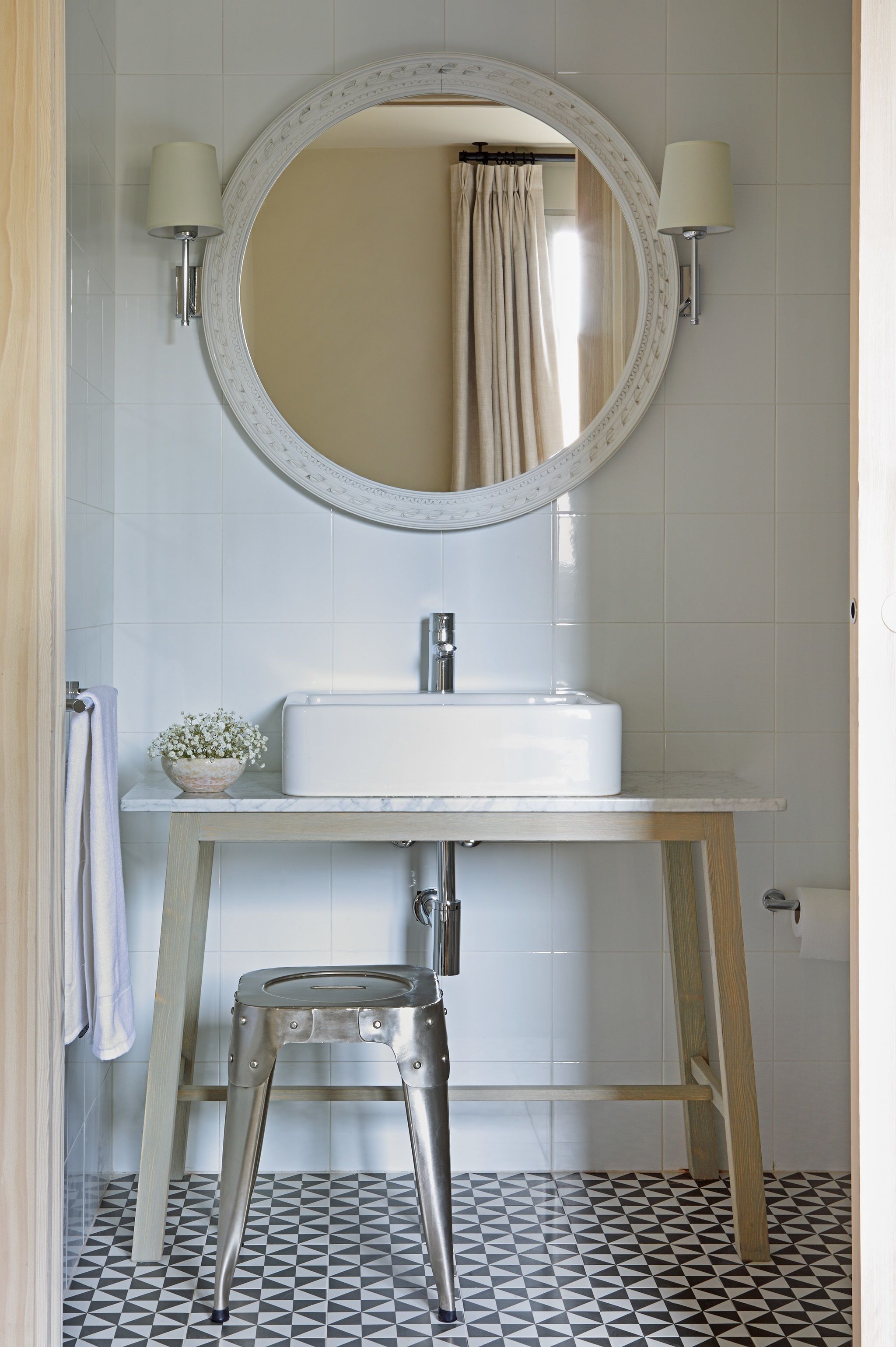 A bathroom with a white sink, a round mirror, and a stool.