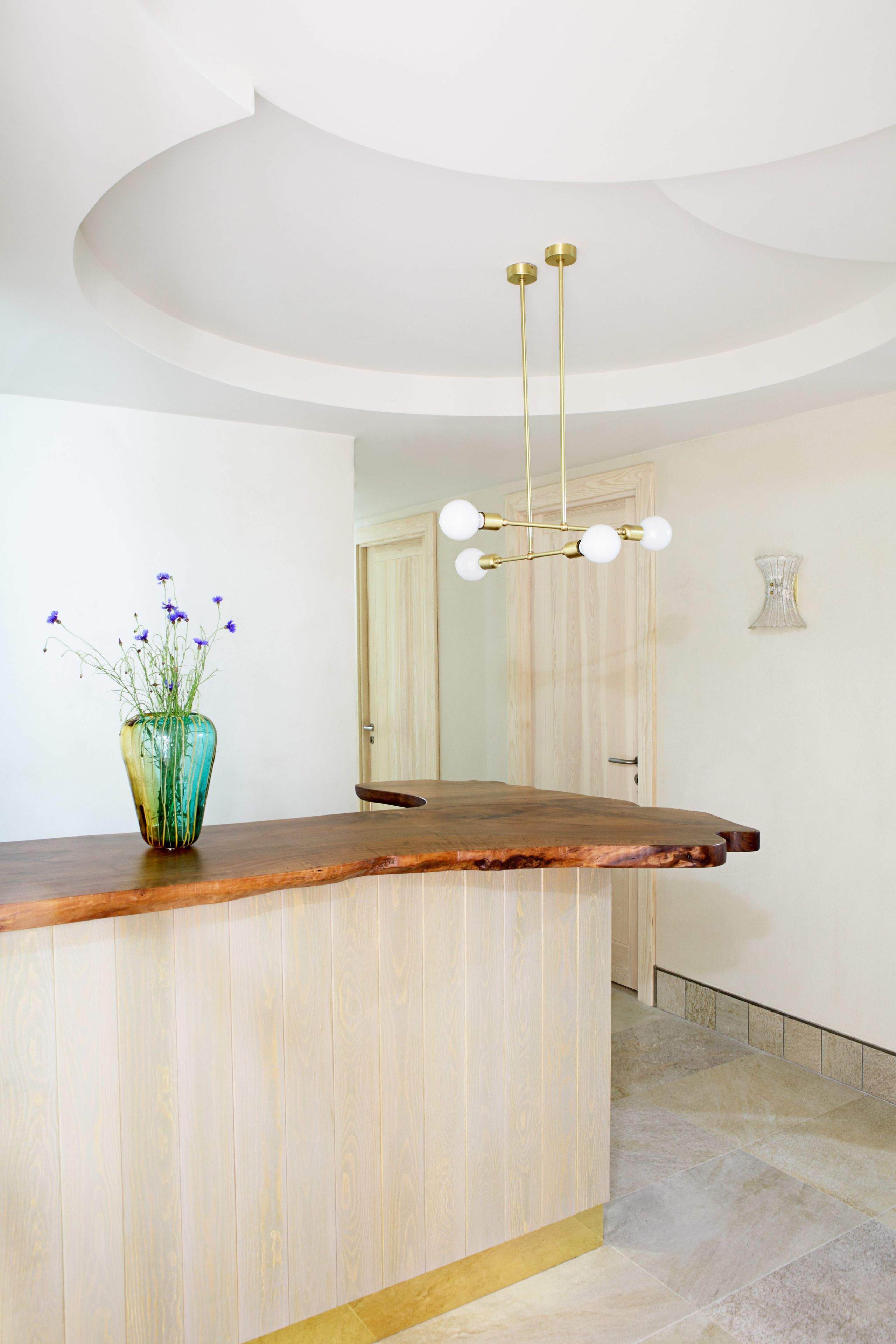 Un comptoir d’accueil avec un plateau en bois, un vase rempli de fleurs et un lustre moderne.