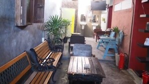 Un pasillo estrecho con bancos y mesas de madera, plantas en macetas y una pared roja con un extintor.