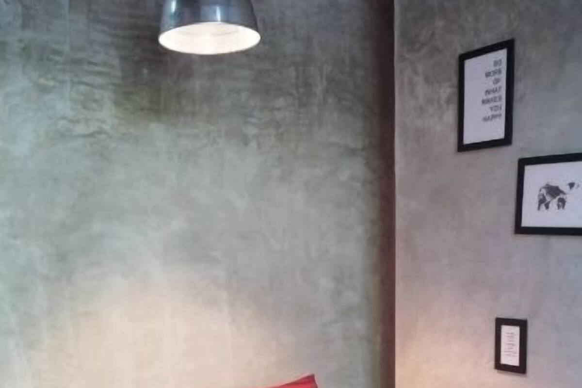 Una cama con ropa de cama roja y una almohada gris, una lámpara de pared y cuadros en la pared.