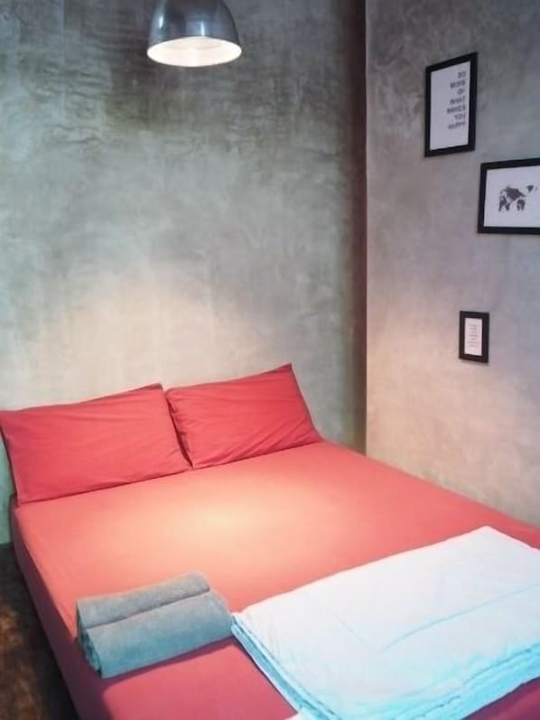 A bed with red bedding and a grey pillow, a wall-mounted light fixture, and framed pictures on the wall.