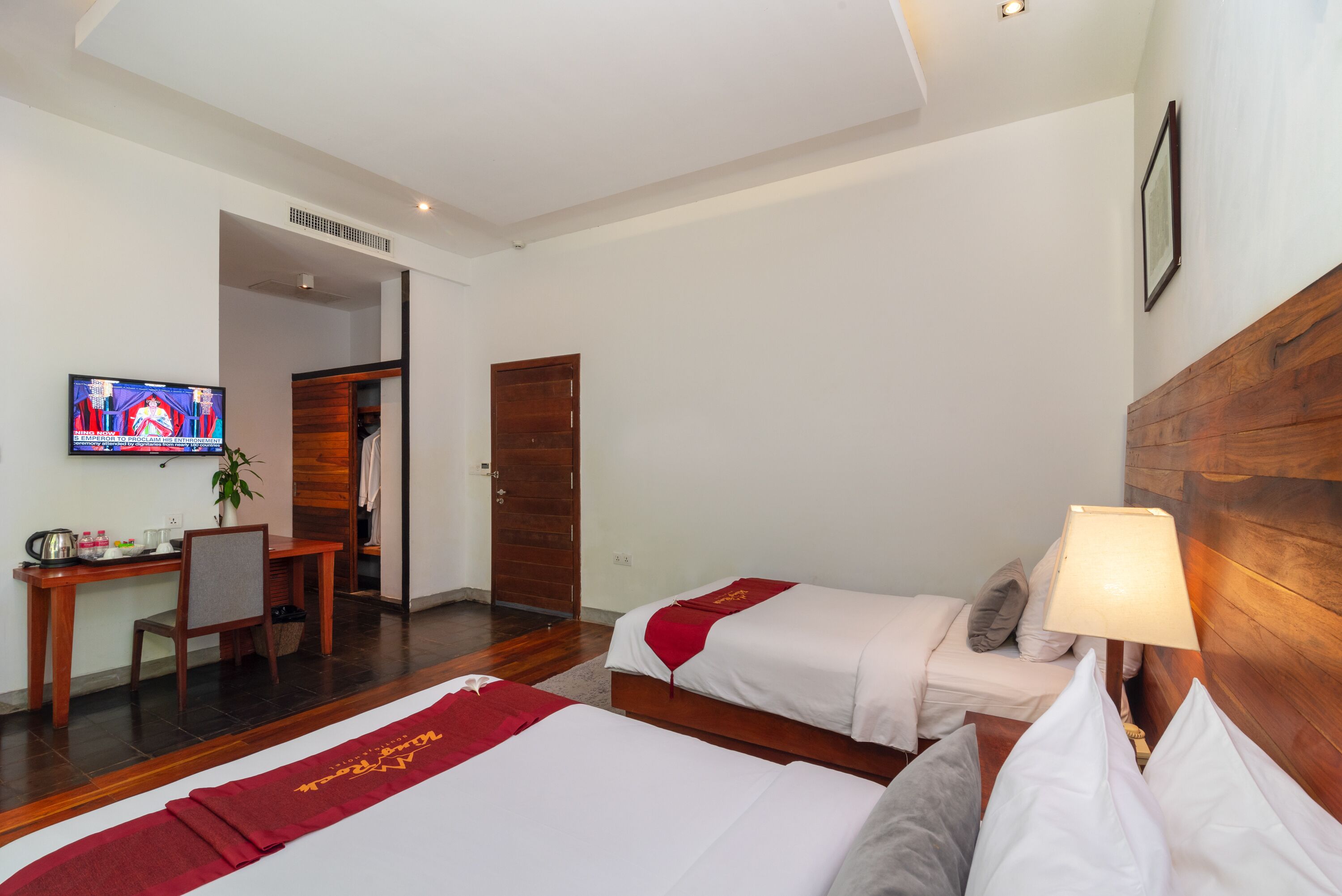 A hotel room with two beds, a desk, a TV, and a wooden headboard.
