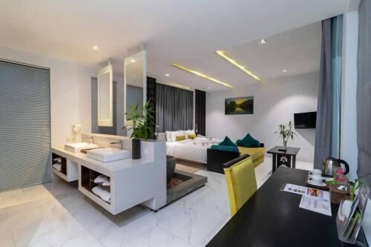 A modern hotel room with a large bed, a sitting area, a desk, and a large window.