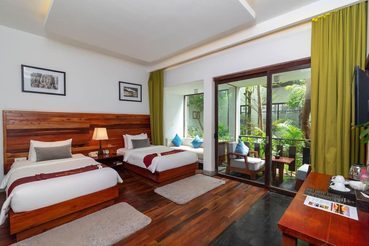 A hotel room with two beds, a wooden headboard, a balcony with plants, and a television.