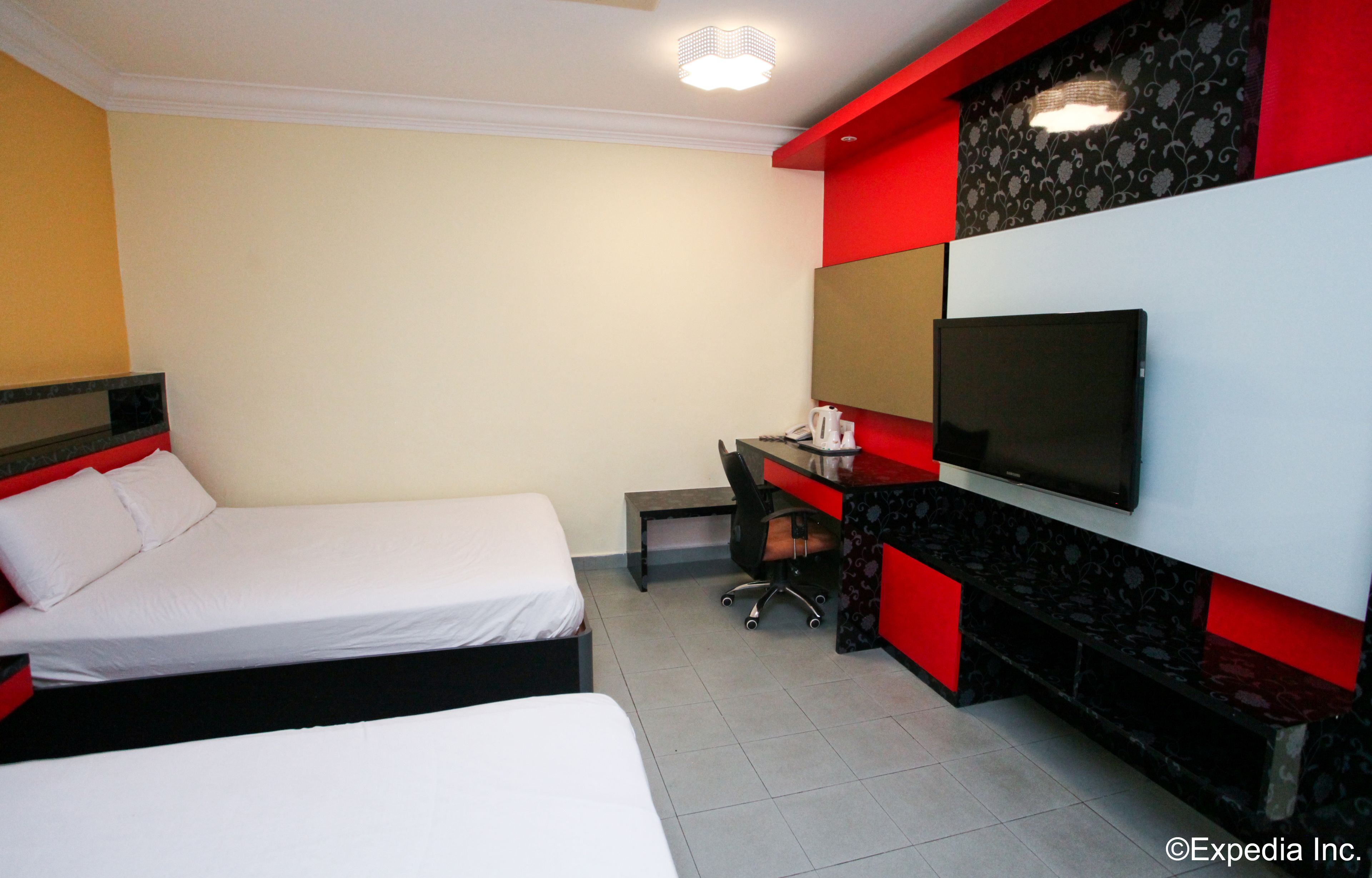 Ein Hotelzimmer mit zwei Betten, einem Schreibtisch, einem Stuhl, einem Fernseher und einem kleinen Tisch.
