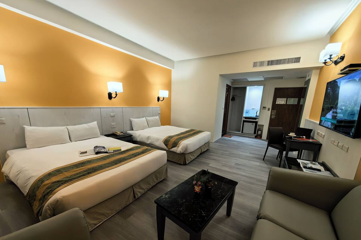 A hotel room with two beds, a TV, a desk, and a seating area.