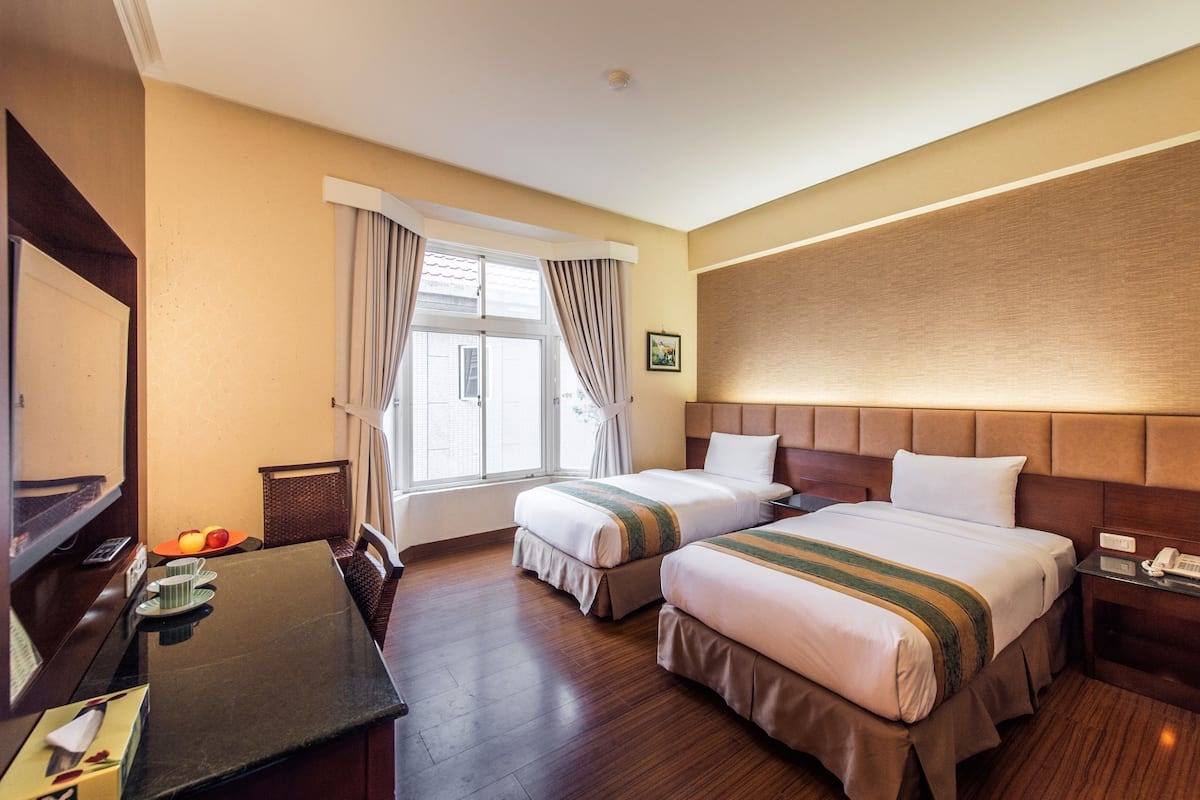 A hotel room with two beds, a desk, a telephone, and a window with curtains.