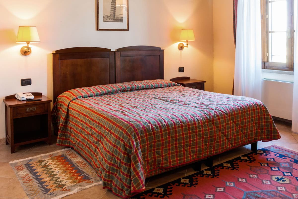 A bedroom with a large bed, two bedside tables, a nightstand, a framed picture on the wall, and a window with curtains.