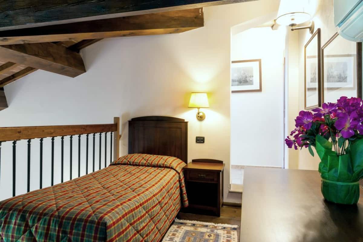 A bedroom with a bed, nightstand, lamp, framed pictures, and a vase of flowers.