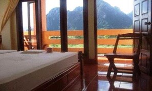 A room with a bed, a chair, and a view of mountains through large windows.