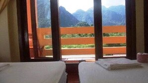Habitación de hotel con dos camas, un balcón con vistas a las montañas y una ventana con cortinas.