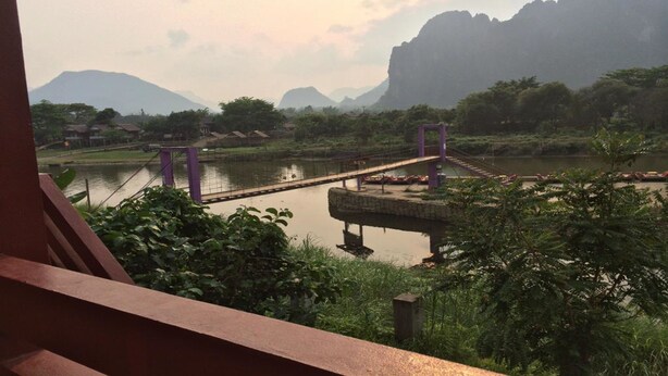 Un río con un puente, rodeado de vegetación y montañas al fondo.