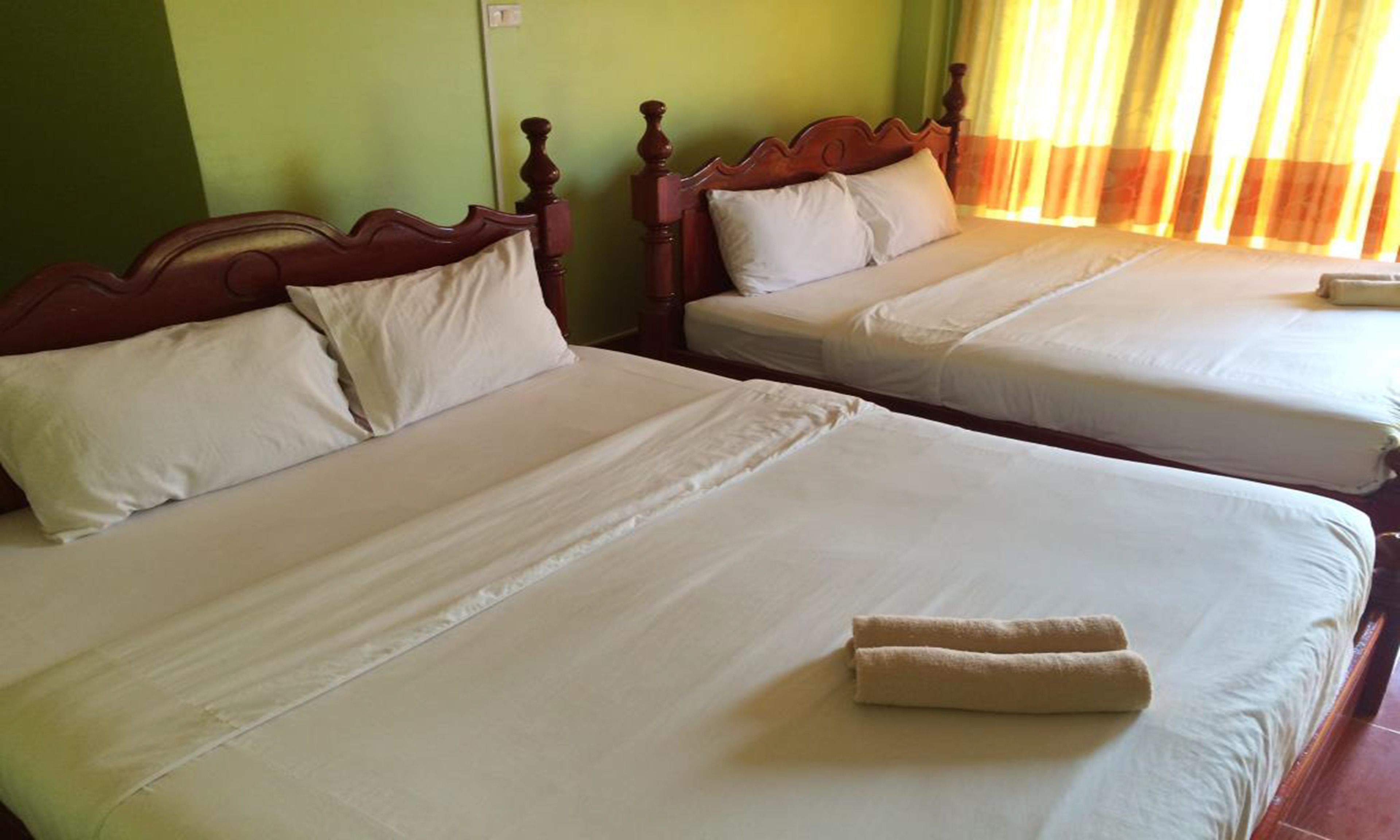 Two twin beds with wooden headboards, white linens, and a rolled towel on the bed.