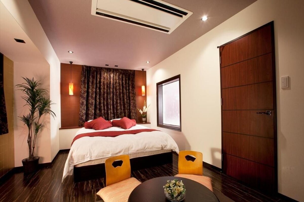 Habitación de hotel con cama, una mesa redonda con un florero, planta en maceta y un armario grande.