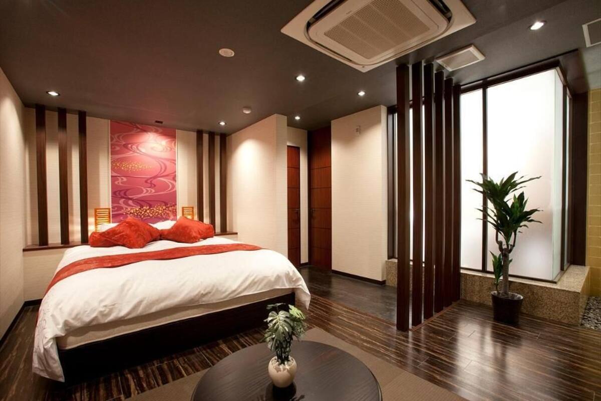 A hotel room with a bed, a round table with a plant, a large window, and a wall-mounted air conditioner.
