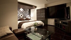 Una habitación de hotel moderna con una cama grande, una mesita de centro de cristal, un televisor y un armario de madera oscura.