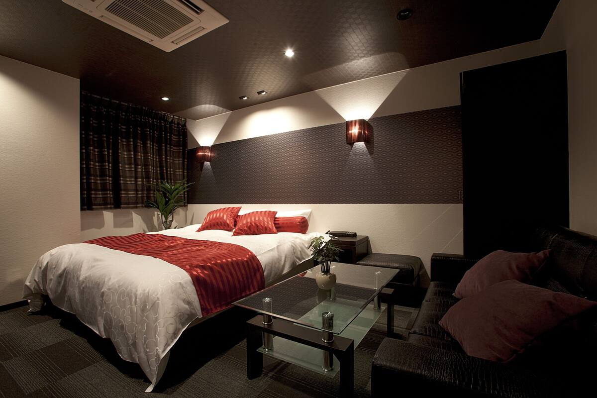A modern hotel room with a large bed, a glass coffee table, a sofa, and a small table with a plant.