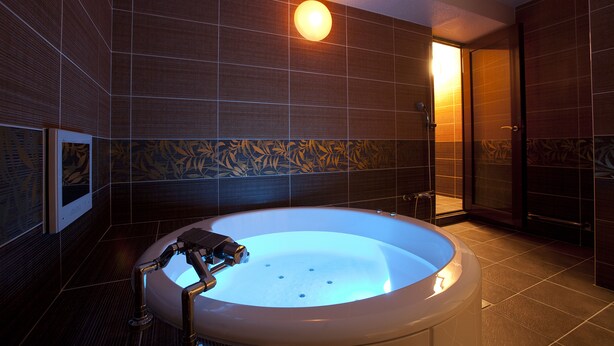 Un baño moderno con una bañera grande, paredes de madera oscura y una zona de ducha visible.