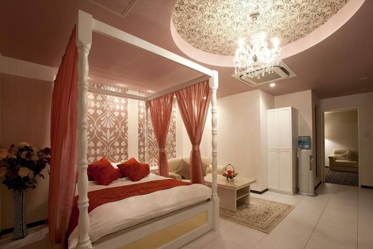 A four-poster bed with a canopy, a chandelier, and a vase of flowers.