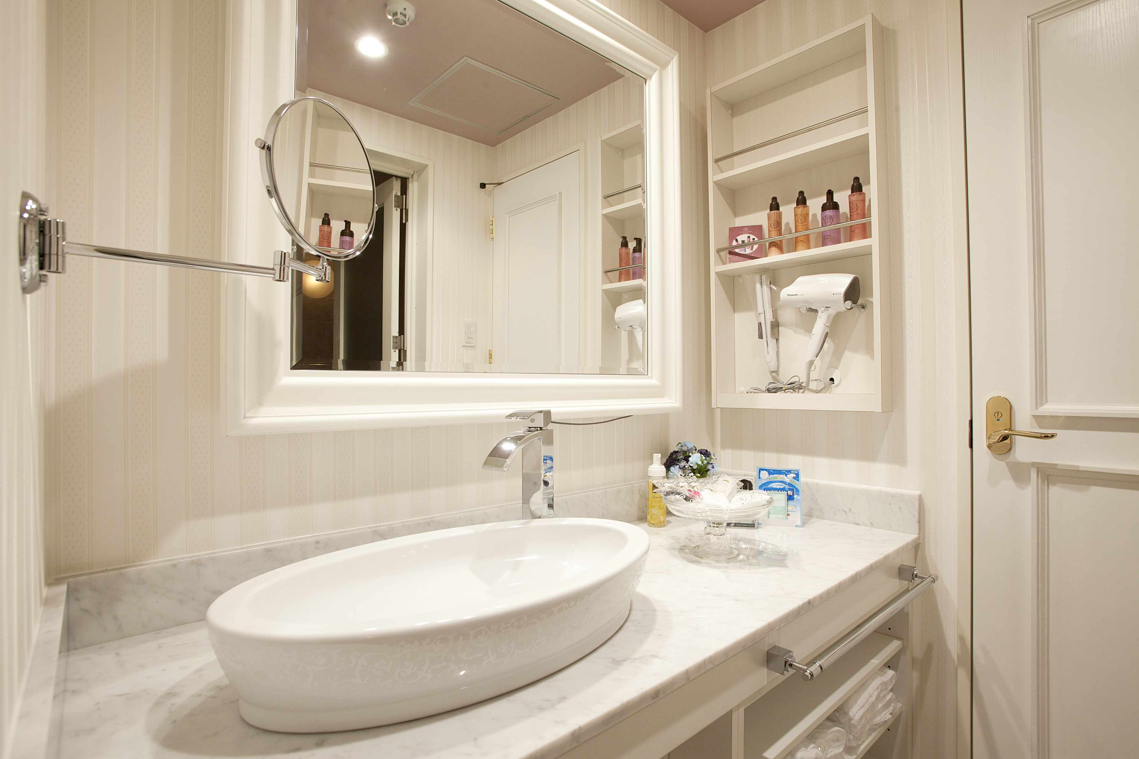A bathroom with a large oval sink, a mirror, and a vanity with shelves holding toiletries.