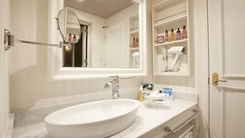 A bathroom with a large oval sink, a mirror, and a vanity with shelves holding toiletries.