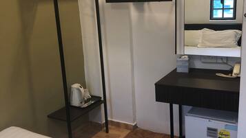 Ein Hotelzimmer mit Bett, Wandfernseher, kleinem Schreibtisch mit Telefon, Kühlschrank und Fenster mit Ausblick.
