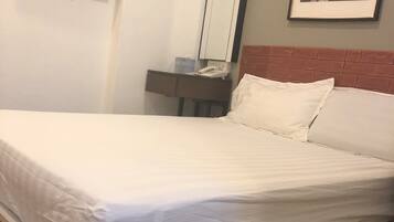 Una cama bien hecha con ropa blanca, un televisor de pantalla plana en la pared, una mesita de noche con un teléfono y un cuadro enmarcado en la pared.