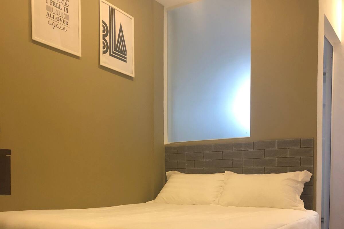 Quarto com cama, cabeceira e duas frases emolduradas na parede.