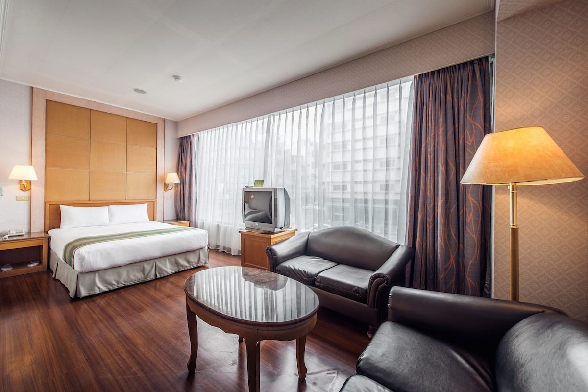 A hotel room with a bed, a sofa, a TV, and a lamp.