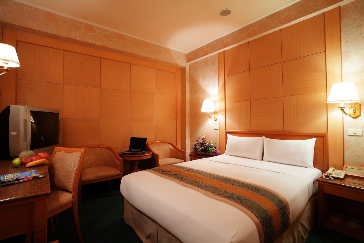 A hotel room with a bed, a desk with a laptop, a chair, a television, and a telephone.