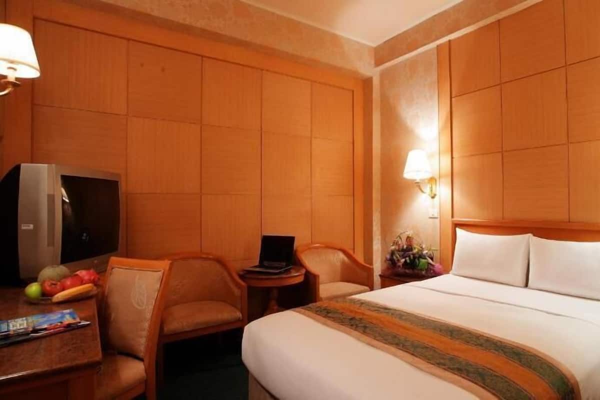 A hotel room with a bed, a desk with a computer, a chair, a television, and a lamp.