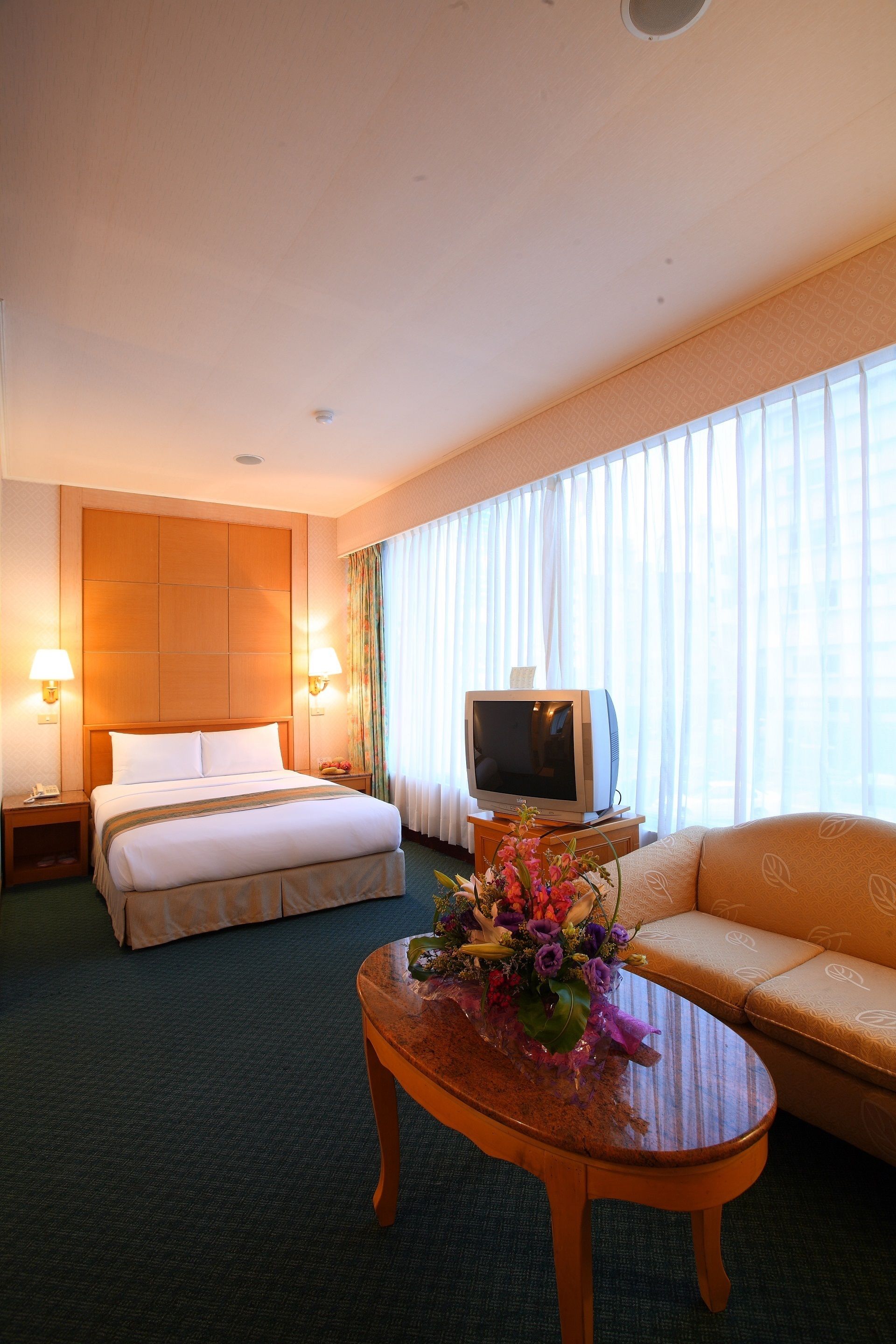 Una habitación de hotel con cama, sofá, televisor y una mesa de centro con flores.