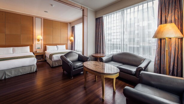 Une chambre d’hôtel avec deux lits, un canapé, une table basse et une lampe.