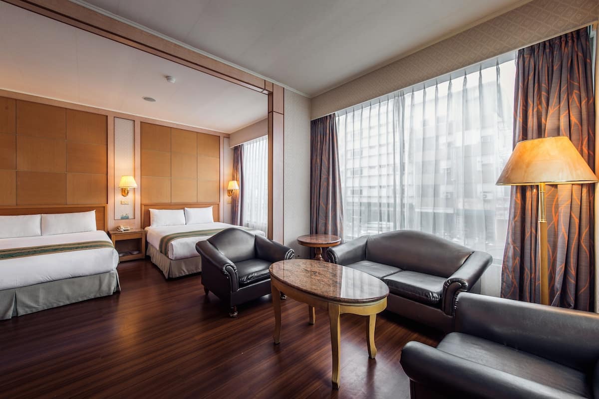 A hotel room with two beds, a sofa, a coffee table, and a lamp.