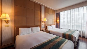 Une chambre d’hôtel avec deux lits, des têtes de lit en bois et une grande fenêtre ornée de rideaux légers.