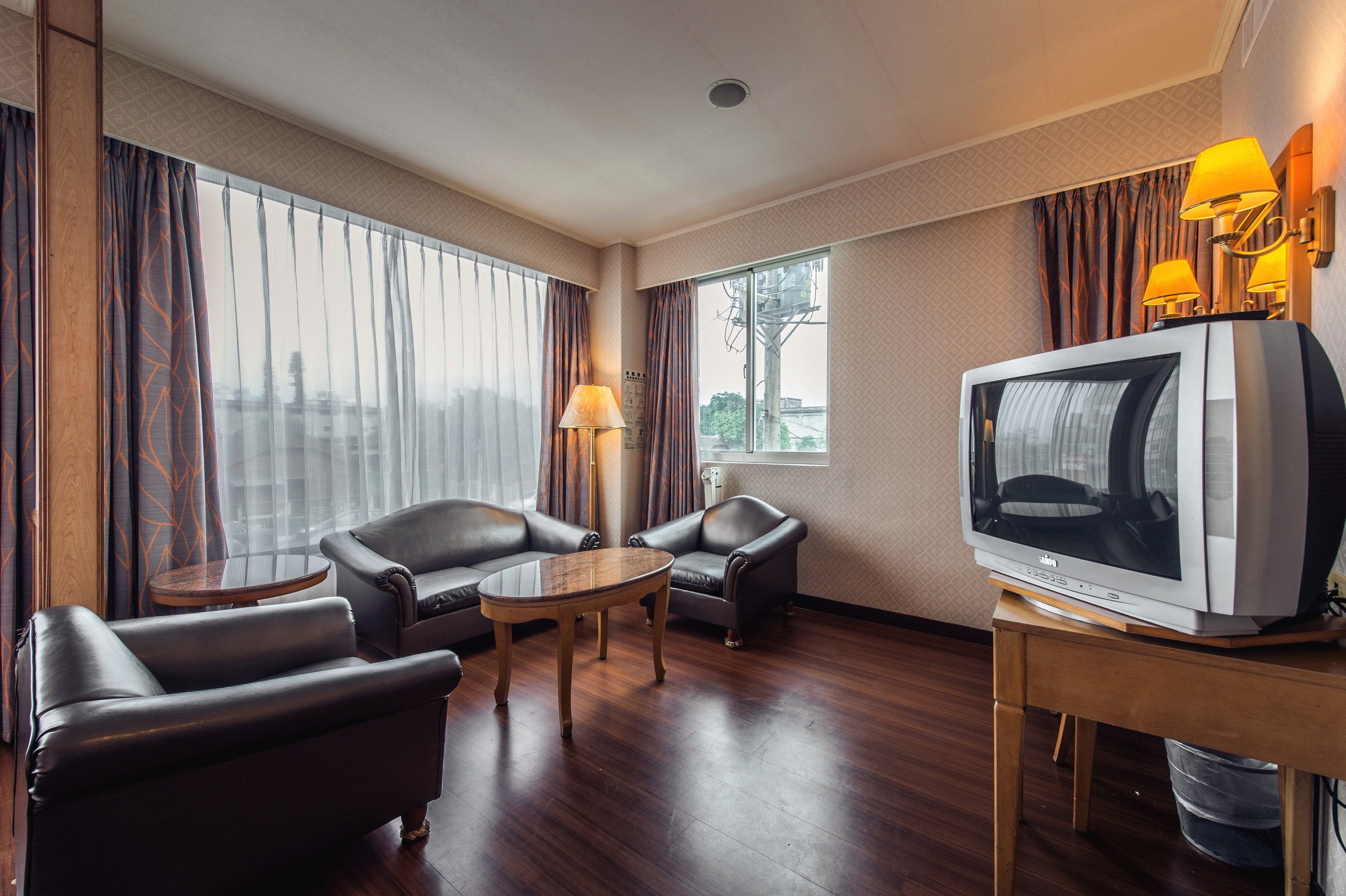 A hotel room with a wooden floor, leather seating, a television, and a lamp.