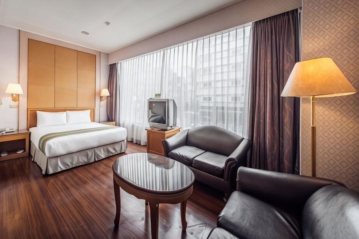 A hotel room with a bed, a TV, a sofa, a coffee table, and a lamp.
