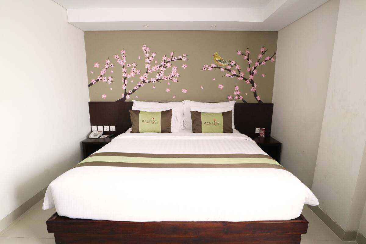 A neatly made bed with a white and brown striped bedspread, two pillows with green tags, and a wall mural of cherry blossoms.